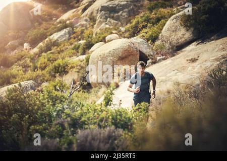 Tackling the mountain trail. Cropped shot of a handsome young man running during his hike in the mountains. Stock Photo