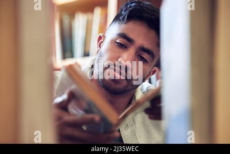 The more pages you turn, the more you learn. Shot of a young man choosing a book to read from a library at college. Stock Photo