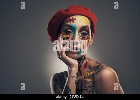 Creativity takes courage. Studio shot of a young woman posing with paint on her face on a grey background. Stock Photo
