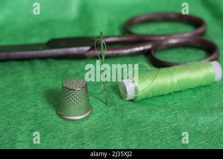 Spool of Green Thread, Thimble and Needle on Green Fabric Close up Stock Photo