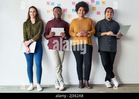Were keeping the connection going strong. Full length shot of a group of a young businesspeople standing together and using their digital devices at Stock Photo