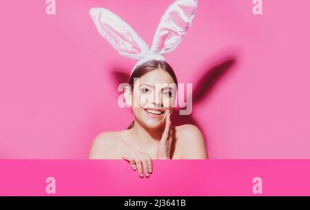Beautiful young woman with bunny ears and pink blank poster. Funny emotions, excited expressing. Stock Photo