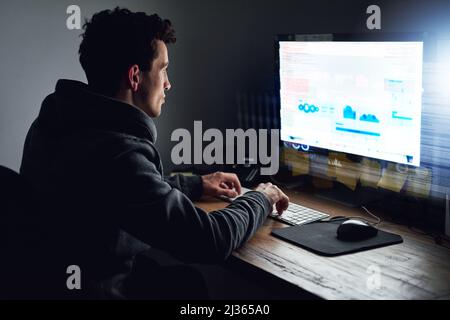 Binary is his second language. Rearview shot of a young programmer working on his computer late at night. Stock Photo
