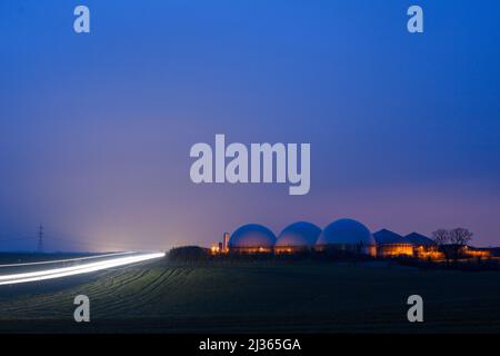 06 April 2022, Saxony-Anhalt, Hohe Börde: A gloomy day dawns over a biogas plant. Next to it, the first commuters drive along a country road. It is supposed to remain cloudy and rainy in the region. It is also supposed to become stormier again. A change in the weather is not in sight. Photo: Klaus-Dietmar Gabbert/dpa/ZB Stock Photo