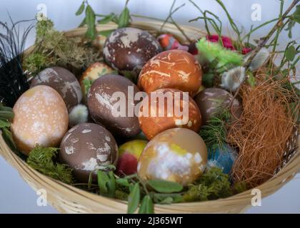 decorated Easter eggs in a wicker basket, European Easter with traditional decoration eggs, easter eggs decorated with natural fresh leaves and boiled Stock Photo