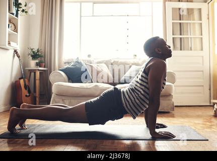 Start your day with some good habits. Shot of a sporty young man doing a cobra stretch while exercising at home. Stock Photo