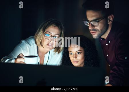 The night shift team knows how to get things done. Shot of a group of colleagues using a computer together during a late night at work. Stock Photo