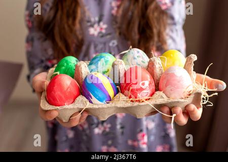 Hands of a girl in a dress holding a cardboard tray with colorful hand-painted eggs Stock Photo