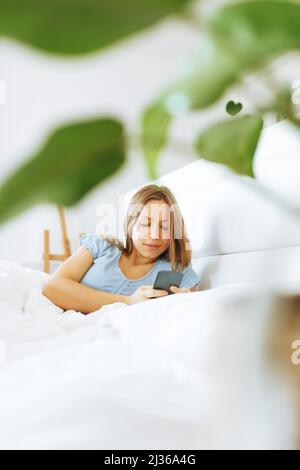 Top view young woman awaken in white cozy bed using smartphone gadget,millennial female wake up lying in bed against home interior background, comfortable bedroom, browsing Internet on in the morning Stock Photo