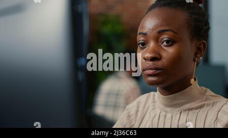 African american software programer working focused looking at computer screen and smiling while typing in it startup office. System engineer coding with algorithms compiling on screens in background. Stock Photo