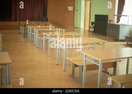 School canteen in Russia. Tables stand in row in hall. Place of public catering. Assembly hall in school. Desks and benches. Stock Photo