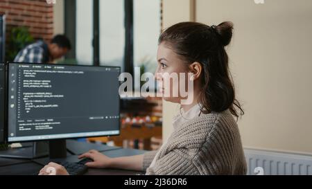 Portrait of focused software engineer writing code looking at multiple computer screens displaying programming language algorithm. Programer coding while colleagues doing teamwork app developing. Stock Photo