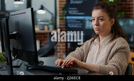 Database programer working focused looking at computer screen while typing in it startup office. App developer writing artificial intelligence code with algorithms compiling on screens in background. Stock Photo