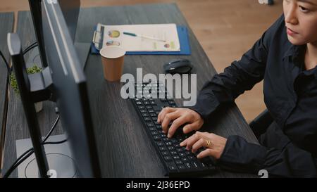 Focus on programer hands typing code on keyboard while looking at computer screens with programming interface. System engineer sitting at desk with clipboard writing algorithm. Stock Photo