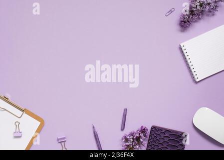Women's desktop close-up, keyboard, notebooks with pen, lilac flowers. Minimal cropped flat composition on a pink background. Copy space Stock Photo