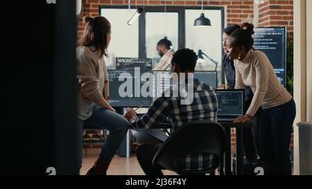 Software programmers discussing about online cloud computing while the rest of the team joins in front of multiple screens compiling code. Coders doing teamwork looking at running algorithms. Stock Photo