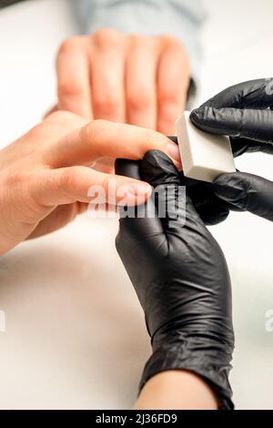 Close up of the caucasian hands of a professional manicurist are filing the nails of a young woman. Young caucasian woman receiving a manicure by a beautician with a nail file in a nail salon Stock Photo