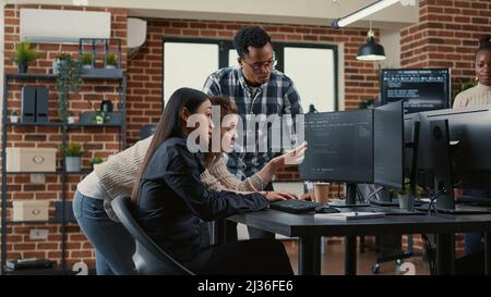 Mixed team of software engineers brainstorming ideas for new cloud computing user interface looking at running code on computer screens. Programmers collaborating on group project compiling algorithm. Stock Photo