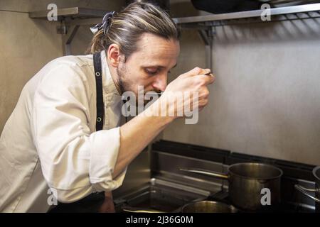 A professional Caucasian chef tasting the food he prepares in the restaurant Stock Photo