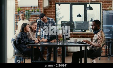 Junior developers collaborating on group project compiling algorithm asking senior programer for help while intern joins the discussion. Software engineers brainstorming ideas looking at screens. Stock Photo
