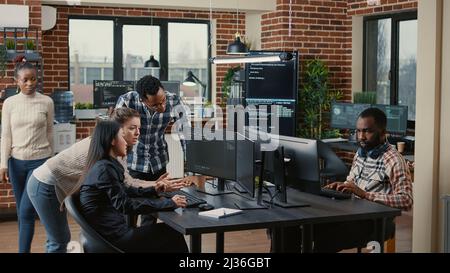 Junior dev programmers collaborating on group project compiling algorithm asking senior developer for help while intern joins the discussion. Software engineers brainstorming ideas looking at screens. Stock Photo
