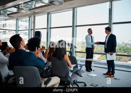 Congratulations on a job well done. Full length shot of two businessmen shaking hands in front of an audience during a seminar. Stock Photo