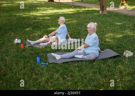Mature man and woman do yoga exercises sitting on lawn grass Stock Photo