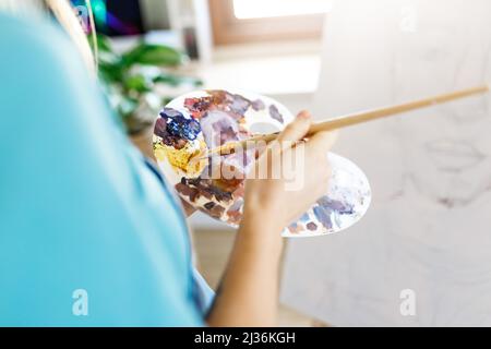 Fine art school. Closeup of artist portrait ,hands holding wooden palette, mixing acrylic paint with brush.Artist woman with paint palette.Hand with brush painting.  Stock Photo