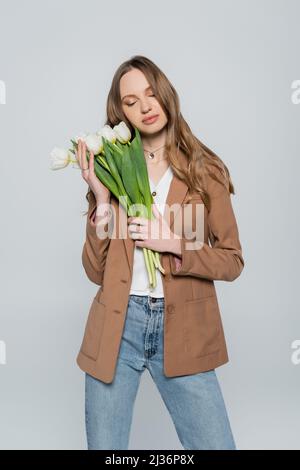 stylish woman with closed eyes posing with tulips isolated on grey Stock Photo