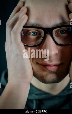 portrait of a young bald man with black eyeglasses holding his head in his hands Stock Photo