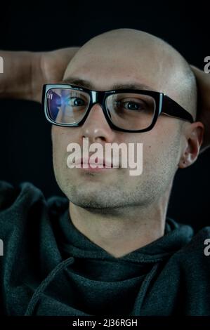 Portrait of a young bald blue-eyed man in black glasses with his hands behind his head who is relaxing Stock Photo