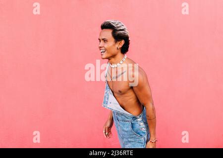 Side view of young happy man in casuals laughing while standing at wall Stock Photo