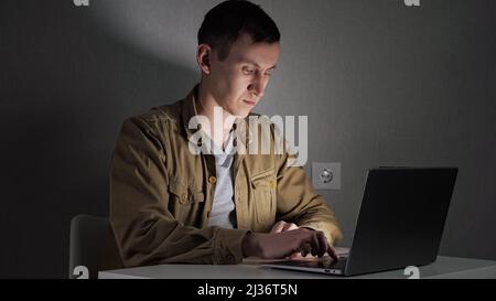 Young man freelancer works at night typing text on laptop Stock Photo