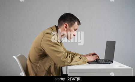 Man employee with crooked neck works on laptop in office Stock Photo