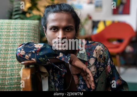 Horizontal medium close-up portrait of handsome androgynous young Indian man wearing shirt with floral pattern looking at camera Stock Photo