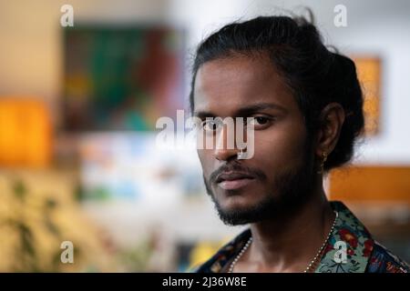 Close-up portrait of handsome non-binary young man of Indian ethnicity with beard on face, long hair and nose pierced looking at camera Stock Photo