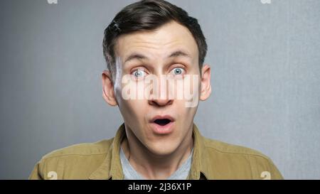 Handsome guy with stylish hairdo surprised to camera over grey background. Stock Photo