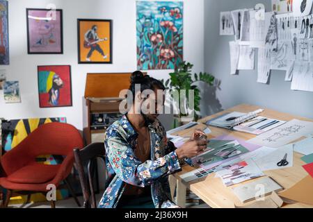 Handsome creative young Indian man wearing unbuttoned shirt taking photos of collage on smartphone camera Stock Photo