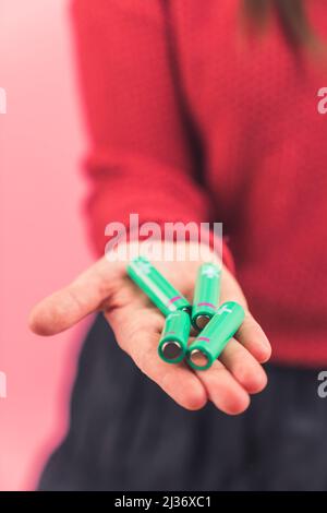 Caucasian woman holding batteries in her hand, no face visible, focus on the batteries copy space studio shot pink background . High quality photo Stock Photo