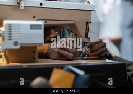 Medium close-up of unrecognizable fashion designer or tailor sitting at table using sewing machine to make new piece of clothing Stock Photo