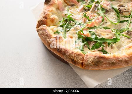Freshly baked crispy pizza with bacon, ham, arugula and cheese. Close up. Copy space. Stock Photo