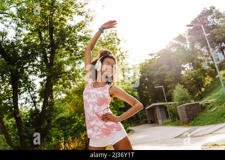 Young black woman in headphones doing exercise while working out outdoors Stock Photo