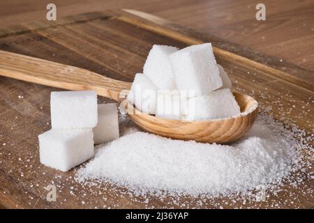 The wooden spoon full of sugar cubes with granulated sugar around on wooden background. Stock Photo