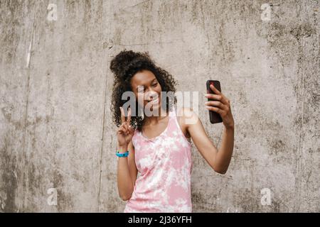 Young black sportswoman taking selfie photo on mobile phone while standing by concrete wall Stock Photo