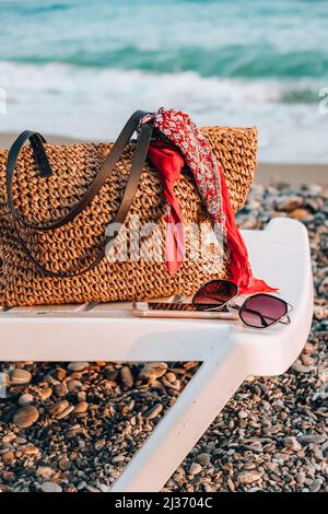 Sun loungers with bag sunglasses and mobile phone in front of sea. Sun chairs on sandy beach. Chaise longue and folded umbrella stand at the edge of t Stock Photo