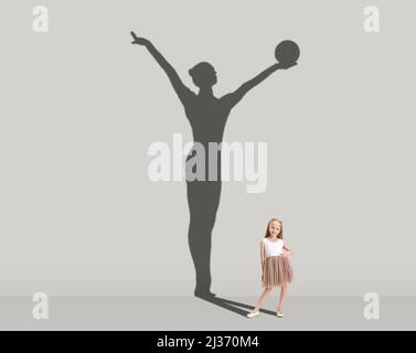 Kids and future. Conceptual image with little girl dreaming about becoming gymnast isolated on studio gray wall. Focus on shadow Stock Photo