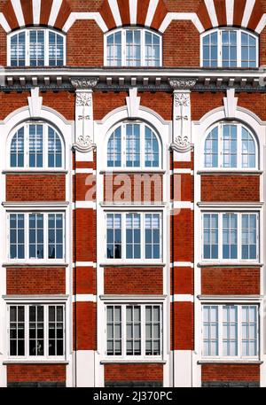 Architectural detail of Victorian building, with red brick, arched windows and decorative plaster work in Art Nouveau style. Geometric background imag Stock Photo