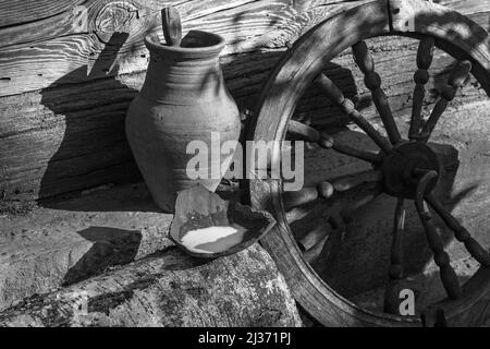 Rustic still life of old items, jug and old wheel on a wooden wall background Stock Photo