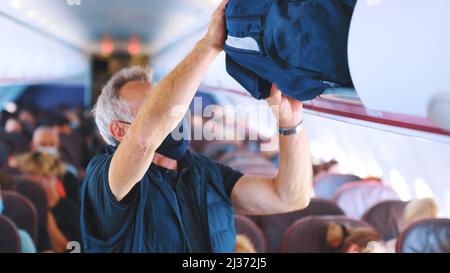 2021.08.18 Mallorca, Spain focus on an elderly man with a mask on his face who puts a travel bag in a box on a plane. High-quality photo Stock Photo