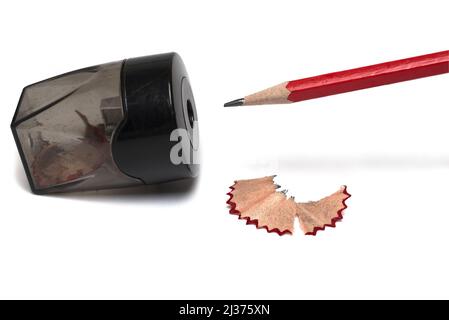 Close up of red sharpened pencil in front of sharpener lying on side next to already scraped wood remains on white background Stock Photo